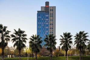 Ein hohes Hotel mit moderner Glasfassade, umgeben von Palmen und einem gepflegten Rasen.