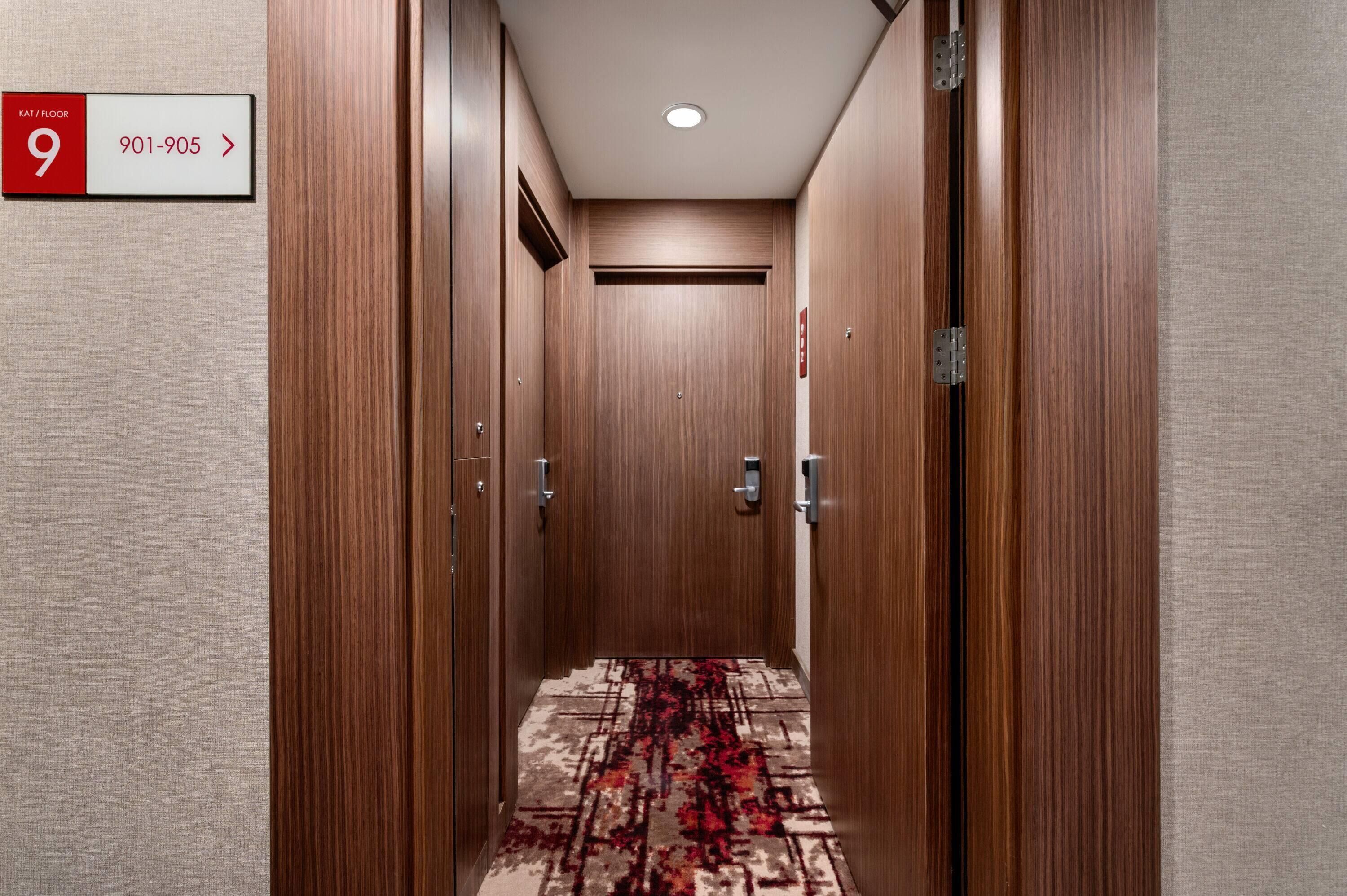 Un couloir d’hôtel aux murs en bois, au sol recouvert de moquette, et une pancarte indiquant la chambre 9, située au neuvième étage.