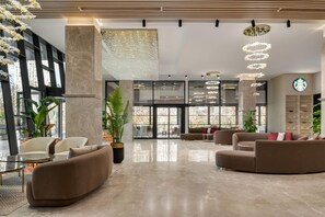 Eine moderne Lobby mit Sitzbereichen und großen Fenstern, mit einem Starbucks-Schild.