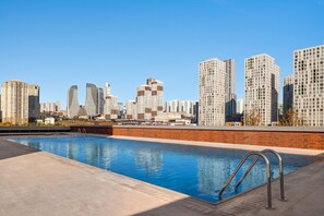 A rooftop swimming pool with a city skyline in the background.