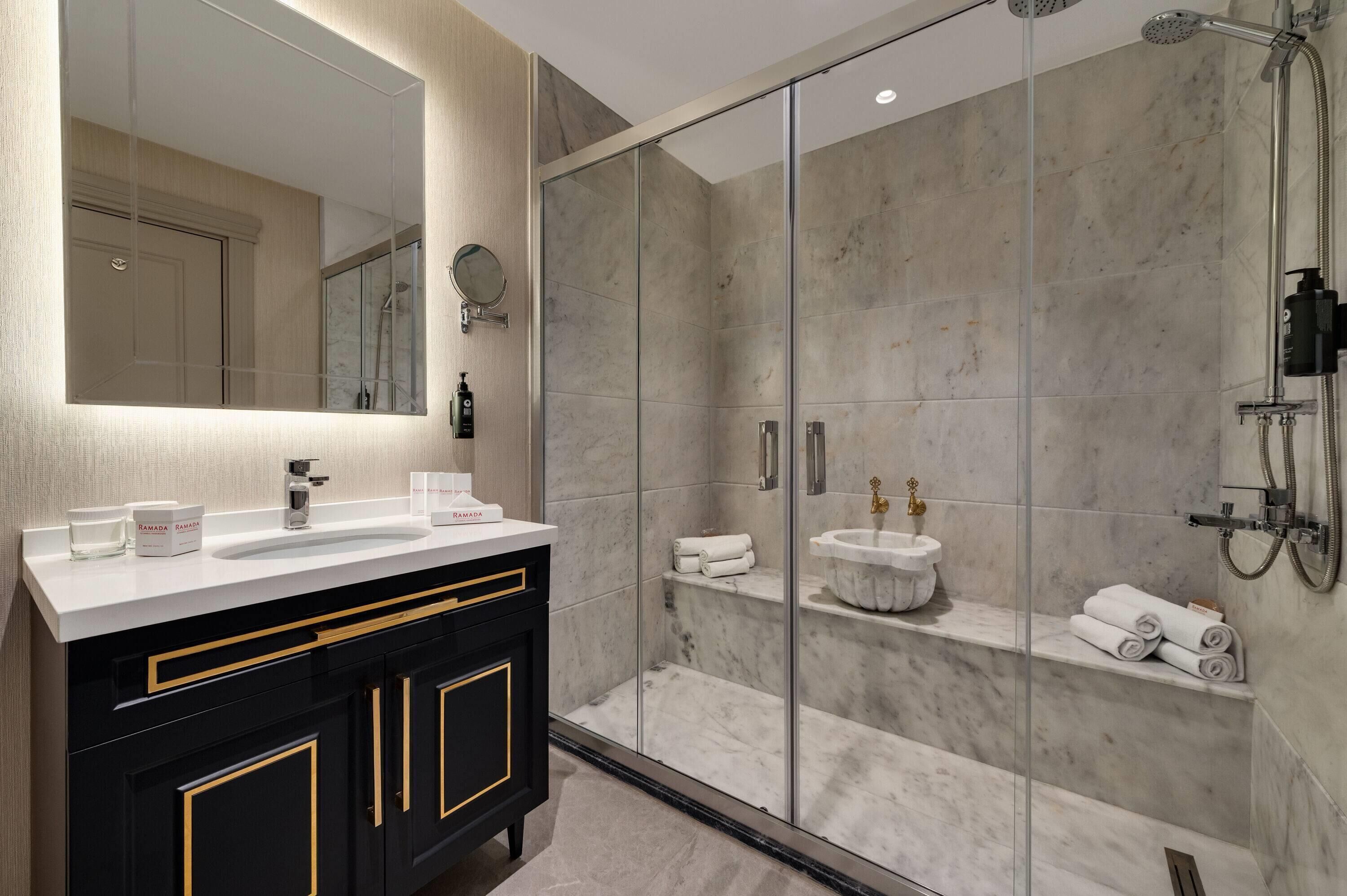 Un bany modern amb dutxa tancada amb vidre, un mirall gran i un lavabo amb taulell blanc.