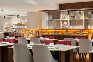 A modern dining area with tables and chairs, a counter with food items, and shelves with books and decorative items.