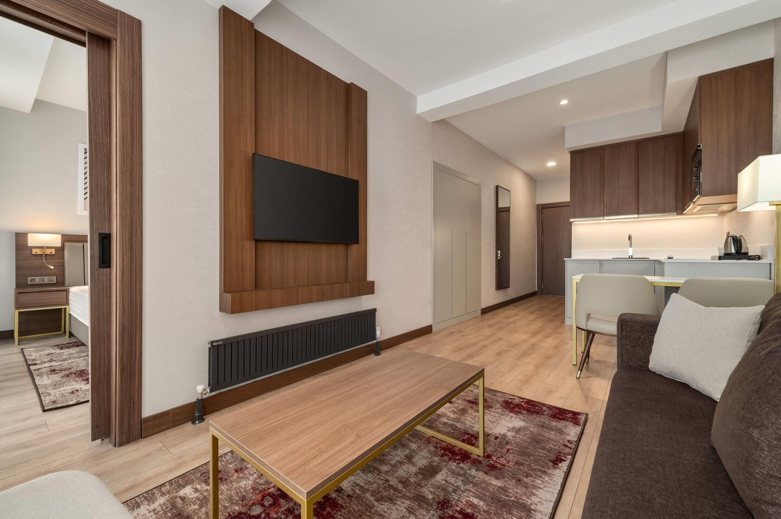 A modern living room with a flat-screen TV, wooden paneling, a dining area, and a kitchen.