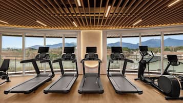 A gym with treadmills and exercise equipment, large windows with a mountain view, and a wooden ceiling design.