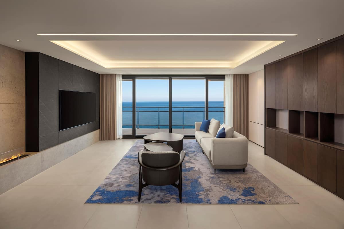 Una sala de estar moderna con televisor grande, un sofá, una mesa de centro y vista al océano.