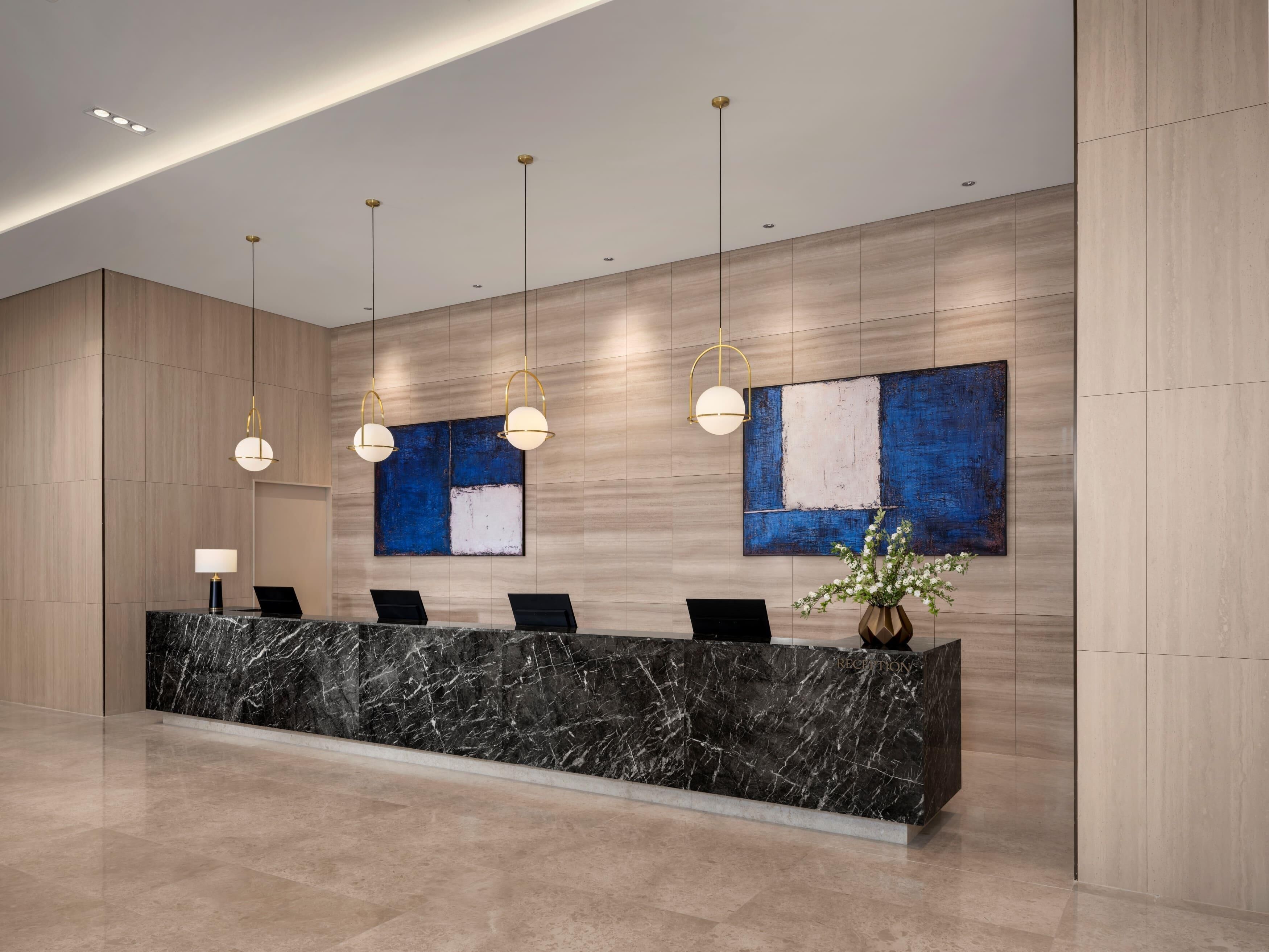 A reception desk with marble top, two black chairs, a vase with white flowers, and two abstract paintings on the wall.