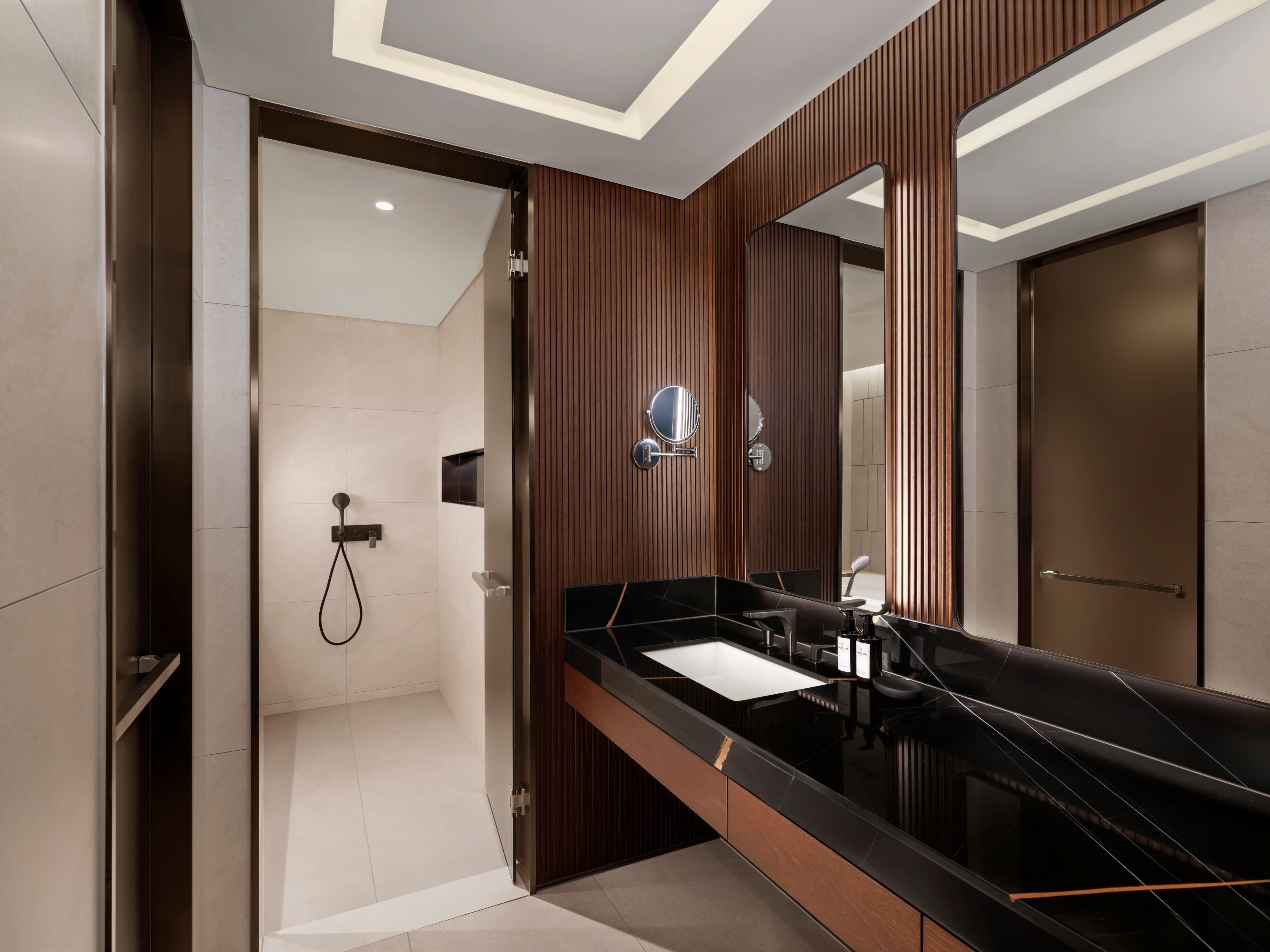 Un baño moderno con encimera negra, un espejo grande y zona de ducha.