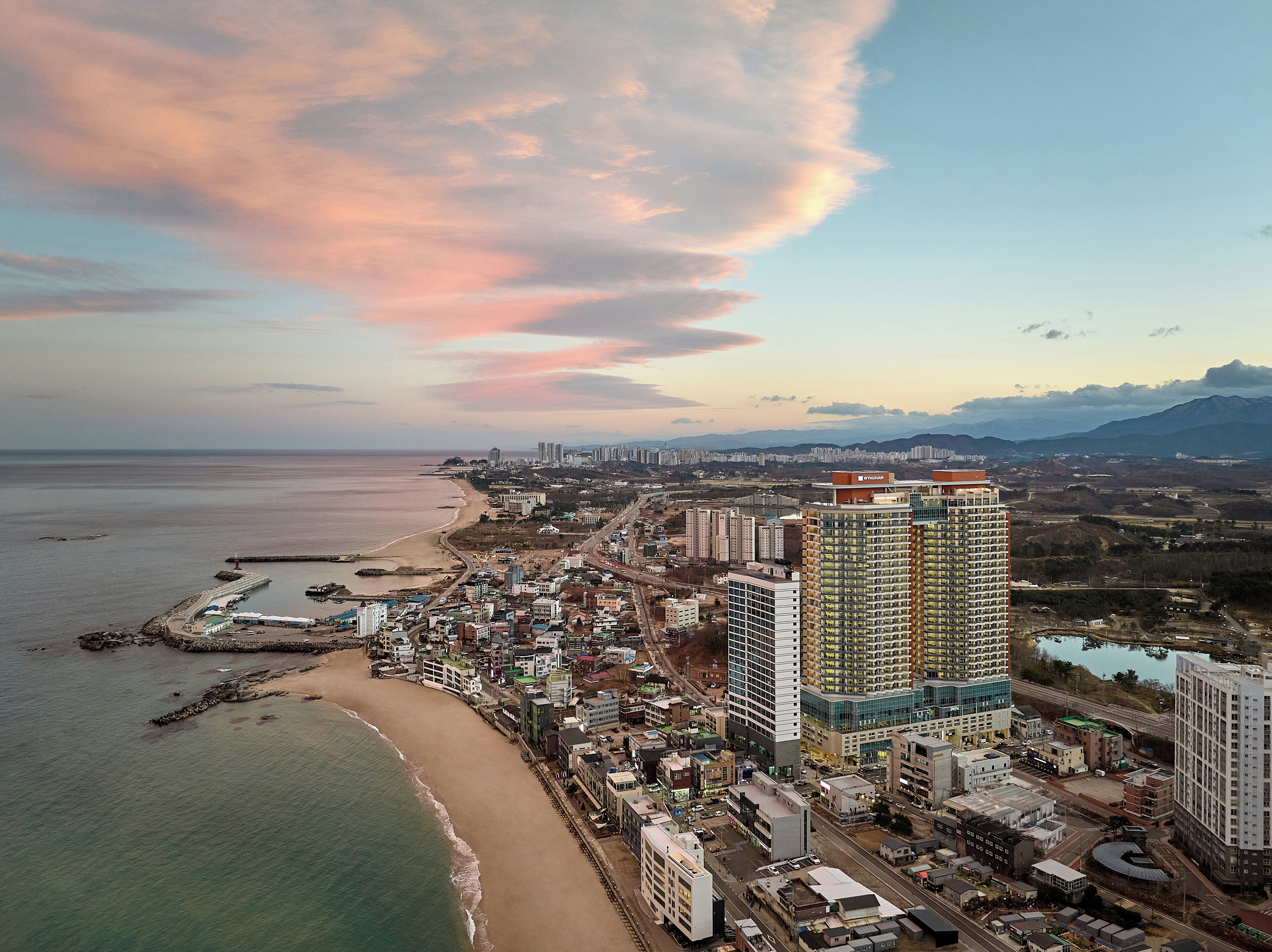 A coastal cityscape with high-rise buildings, a beach, and a pier.
