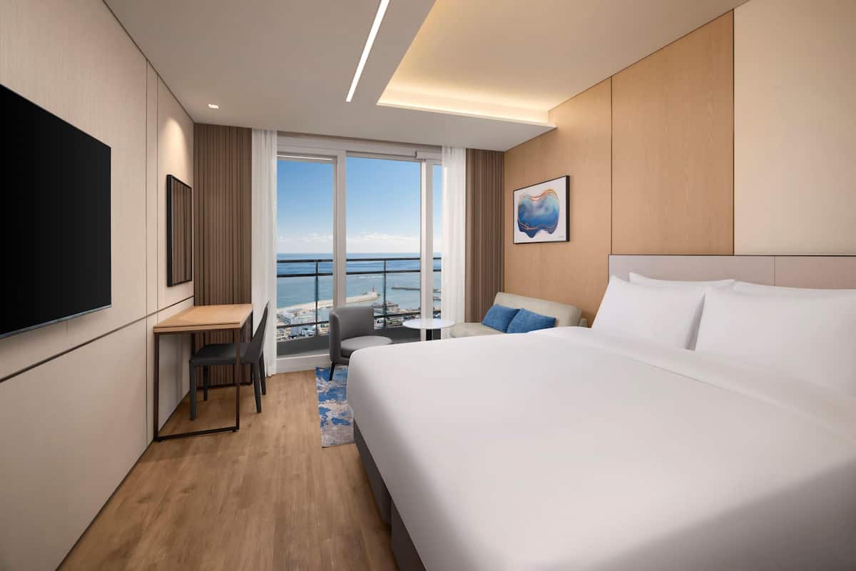 Habitación de hotel con una cama grande, un escritorio, una silla, un televisor y vista al océano.