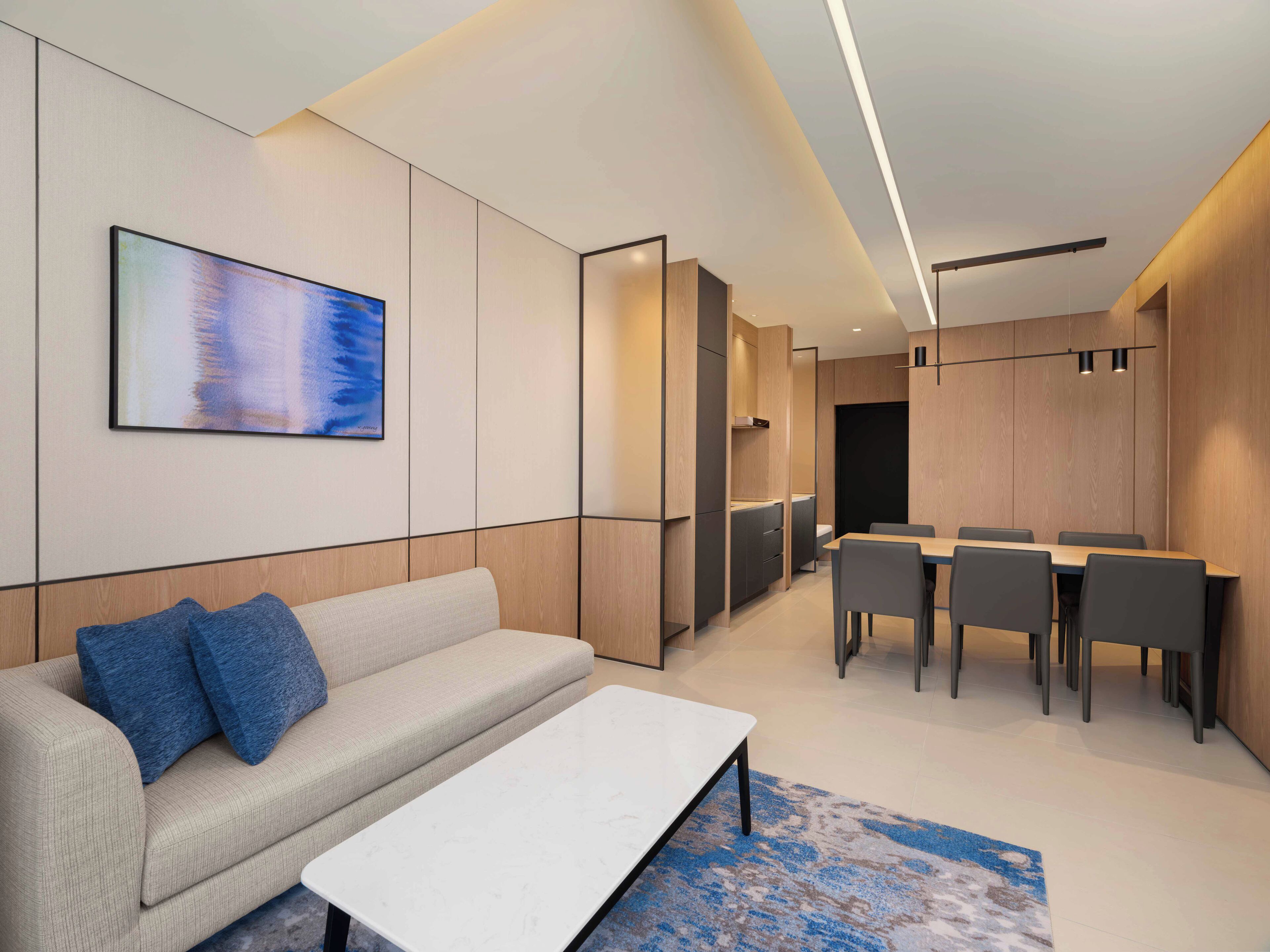Una habitación de hotel moderna con un sofá, una mesa de comedor con sillas, un cuadro en la pared y un armario de madera.