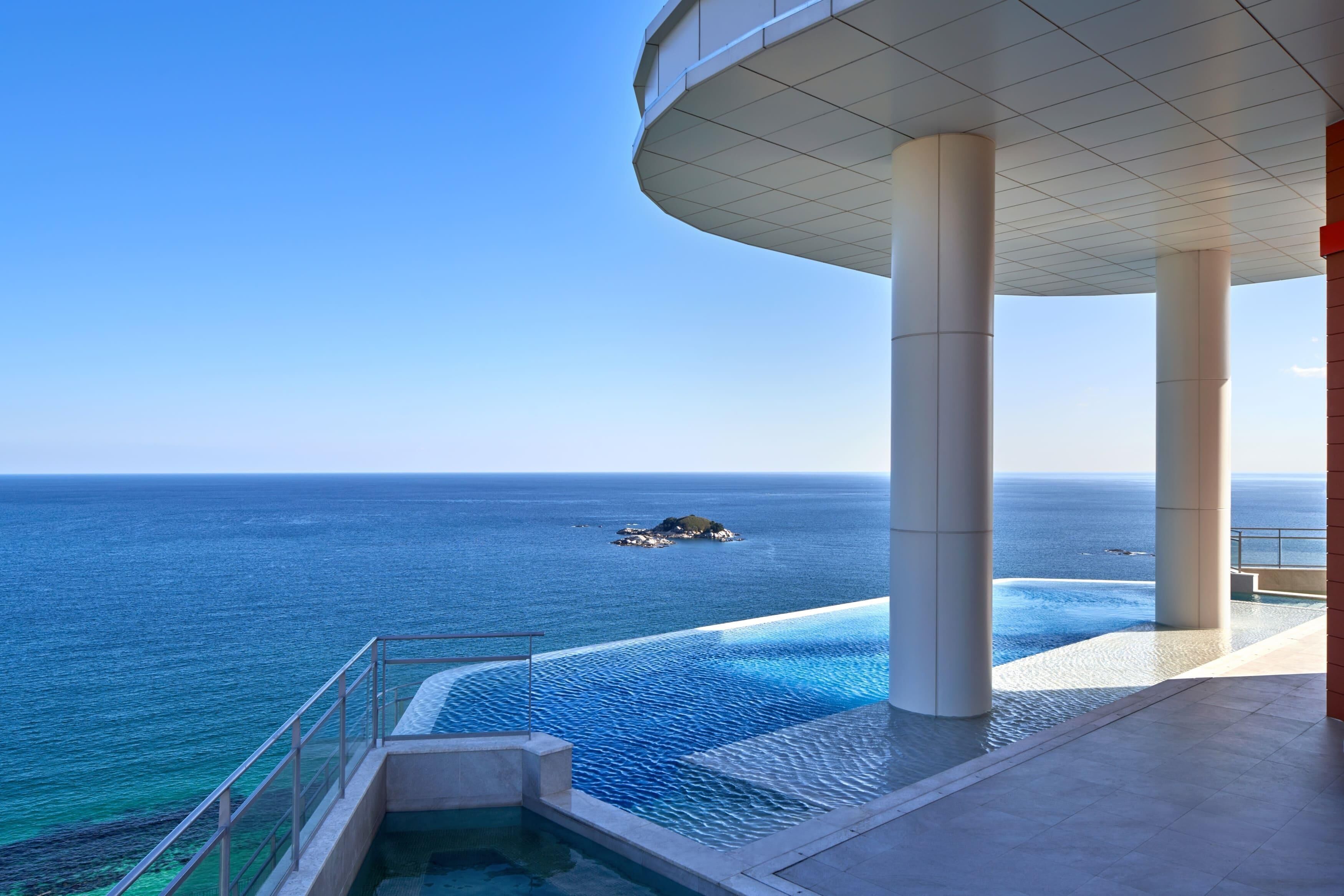 Un hotel moderno con piscina con vistas al océano, grandes columnas y una vista despejada del mar.