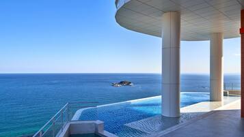 Un hotel moderno con piscina con vistas al océano, grandes columnas y una vista despejada del mar.