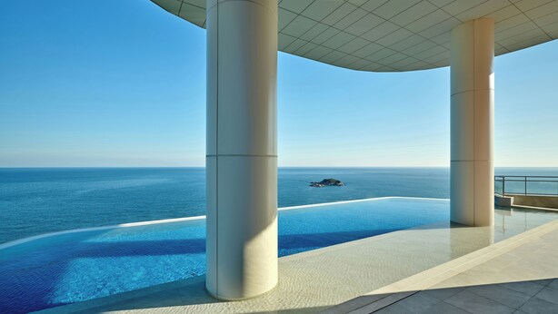 A modern infinity pool with a clear view of the ocean and a distant island.