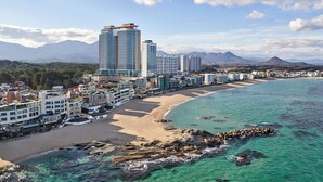 A coastal cityscape with high-rise buildings, a sandy beach, and clear turquoise waters.