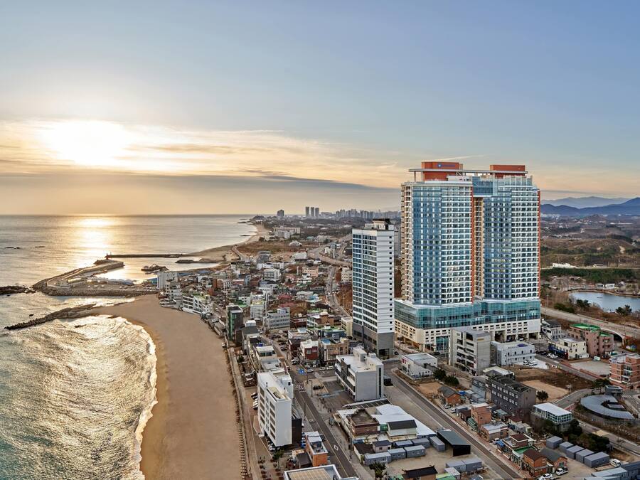 A coastal cityscape with high-rise buildings, a beach, and a sunset.
