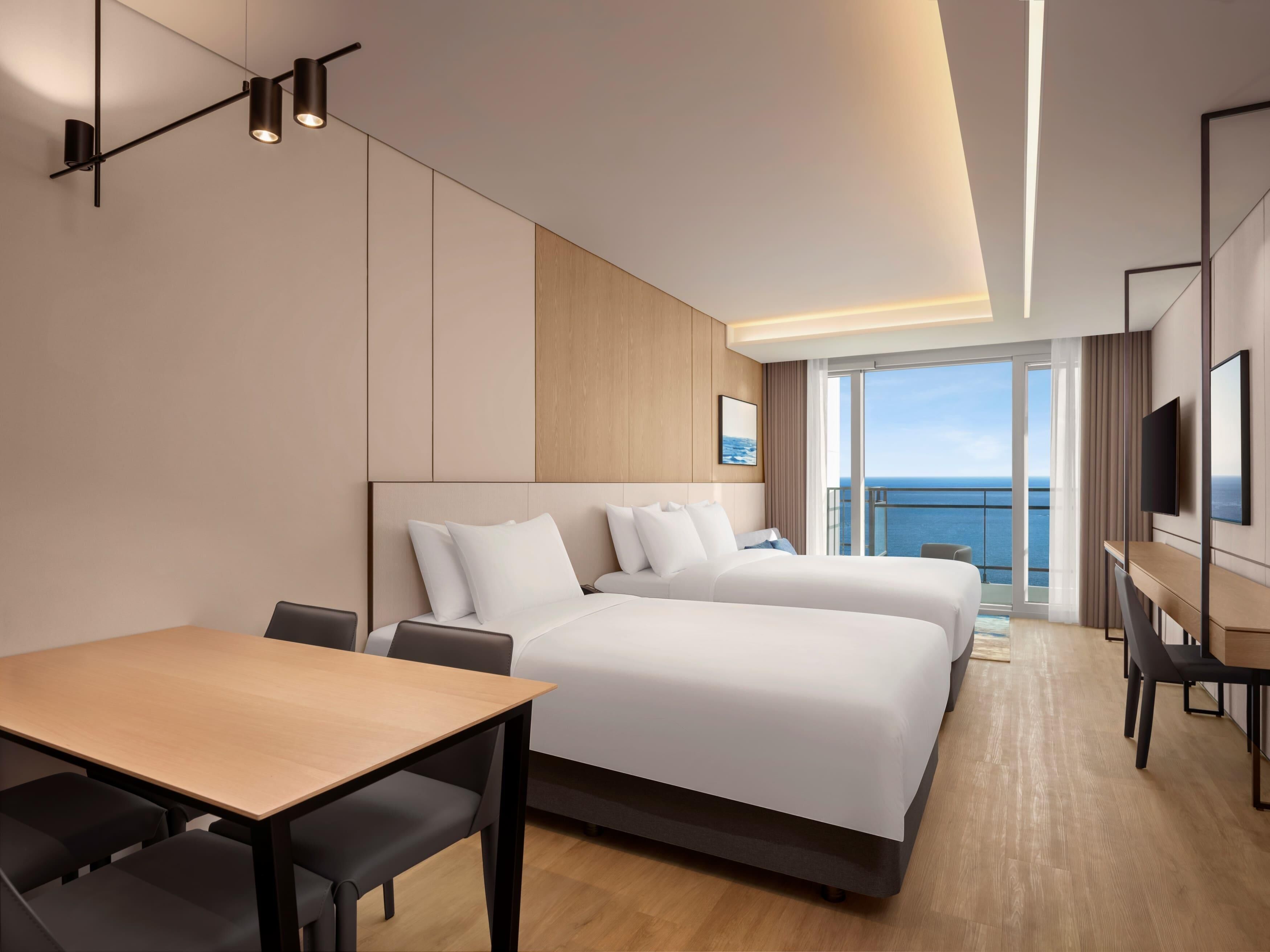 A hotel room with a large bed, a desk, and a view of the sea.