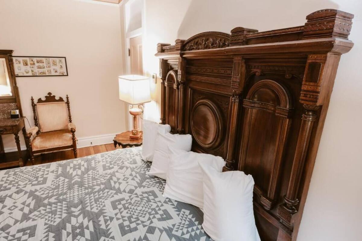 A bedroom with a large bed, a wooden headboard, a chair, a lamp, and a framed picture on the wall.