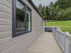 A wooden deck with a white railing, a large window, and a view of a green landscape. - Cedar Lodge 2 Bedrooms With hot tub (Northwich)