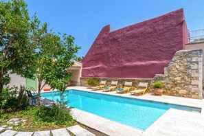A swimming pool with lounge chairs, a stone wall, and a large pink structure. - Villa Verde Petra - Three Bedroom Villa, Sleeps 6 (Rethymno)