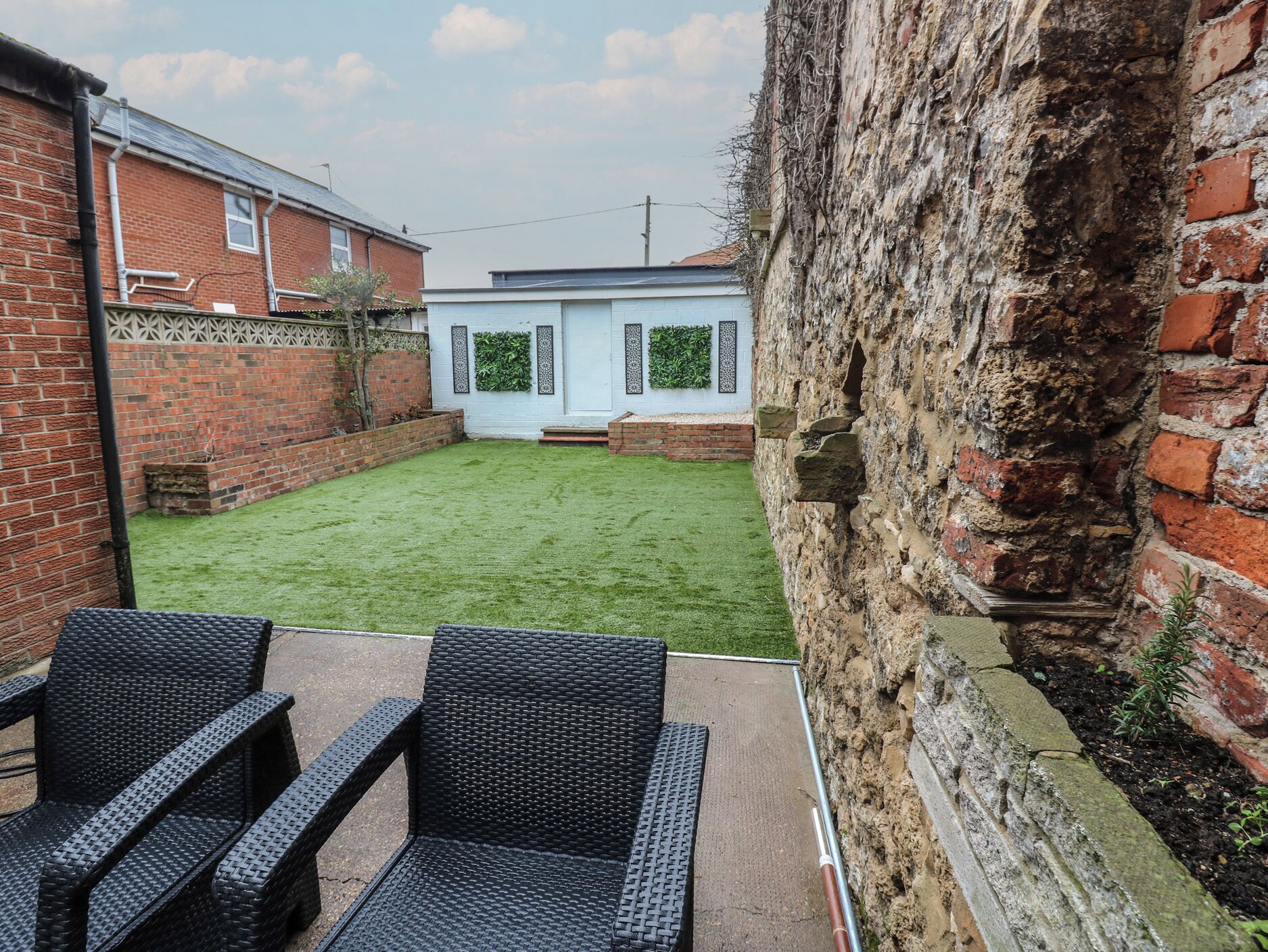 A backyard with a grassy lawn, a white door, and a brick wall.