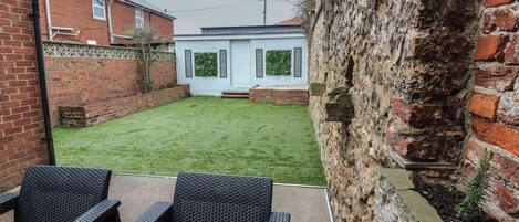 A backyard with a grassy lawn, a white door, and a brick wall.