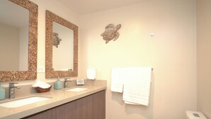 Um banheiro moderno com duas pias, um espelho grande, vaso sanitário e um detalhe decorativo na parede.
