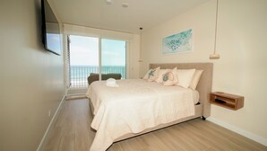 Quarto com cama grande, TV montada, varanda com vista e um quadro na parede.