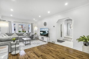 A modern living room with a grey sofa, a flat-screen TV, and a wooden floor. - Romeo & Juliet Niagara Retreat - Clifton Hill & Niagara Falls (Niagara Falls)