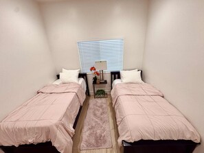 A small, well-lit room with two single beds, a nightstand with a lamp, and a window with blinds. - Charming Newly Built ADU. Perfect for Families (Garden Grove)