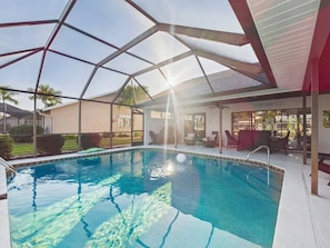 Piscina con cerramiento de vidrio, rodeada de sillones de descanso y un área de patio techada.