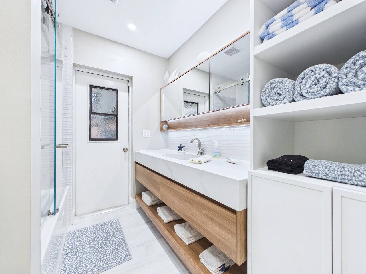 A modern bathroom with a glass shower enclosure, a white vanity with a marble countertop, and a large mirror above the sink.