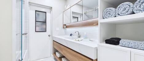 A modern bathroom with a glass shower enclosure, a white vanity with a marble countertop, and a large mirror above the sink.