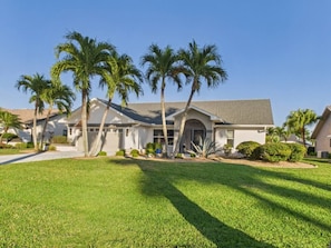 A residential house with a well-maintained lawn, palm trees, and a clear sky. - 3 Bedroom Waterfront Pool Villa with Gulf Access (Cape Coral)