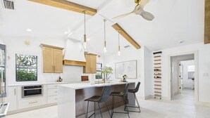 Eine moderne Küche mit Kochinsel, Barhocker, Pendelleuchten und Deckenventilator.