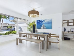 A modern dining area with a table, chairs, a bench, a ceiling fan, and a window with a view of the outside. - 3 Bedroom Waterfront Pool Villa with Gulf Access (Cape Coral)