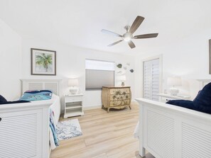 Un dormitorio con cama, mesitas de noche, cómoda, ventilador de techo y ventana.