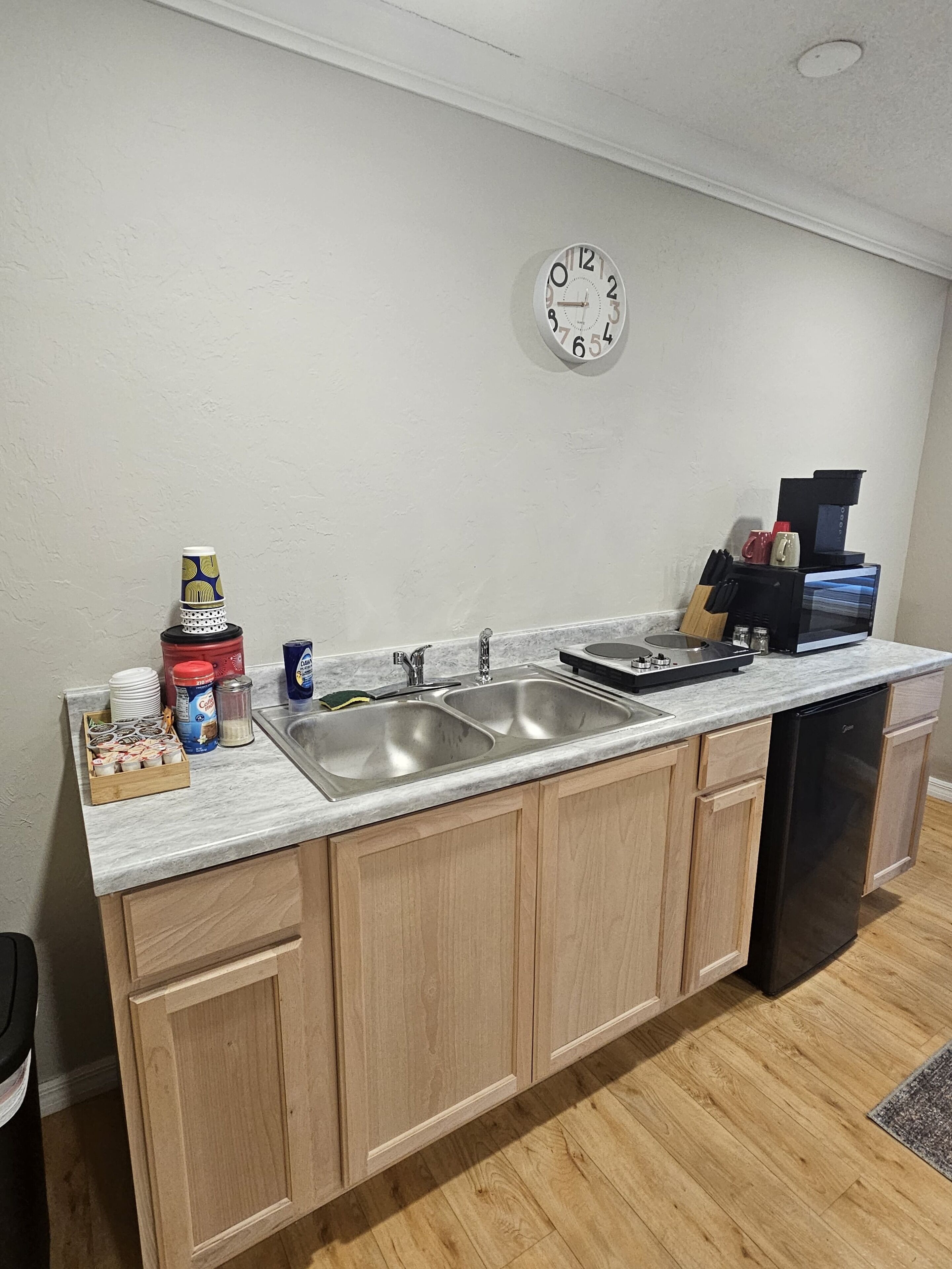 A kitchen with a double sink, wooden cabinets, a coffee maker, and a clock on the wall.