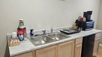 A kitchen with a double sink, wooden cabinets, a coffee maker, and a clock on the wall.