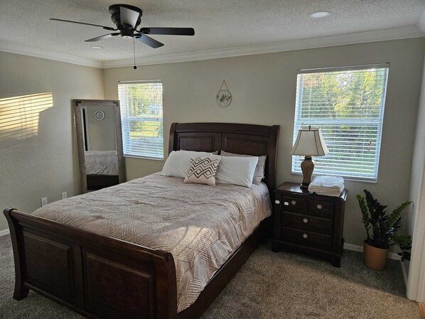 A bedroom with a bed, nightstand, lamp, potted plant, and ceiling fan.