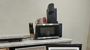 Et lille køkken med indbygget mikroovn, kaffemaskine og køleskab med vandflaske og glas.