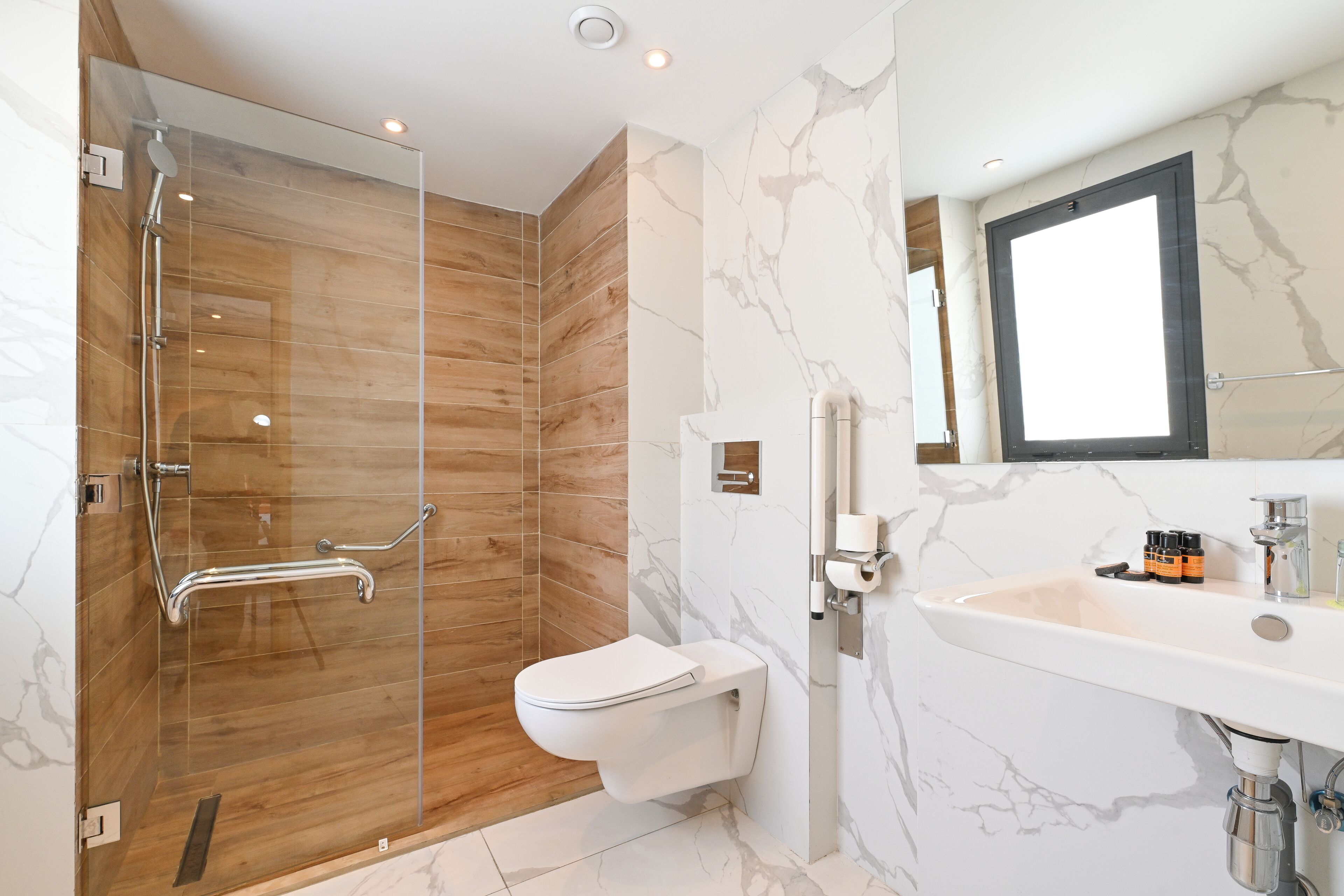 Un baño moderno con ducha de vidrio, inodoro blanco y lavamanos de mármol.