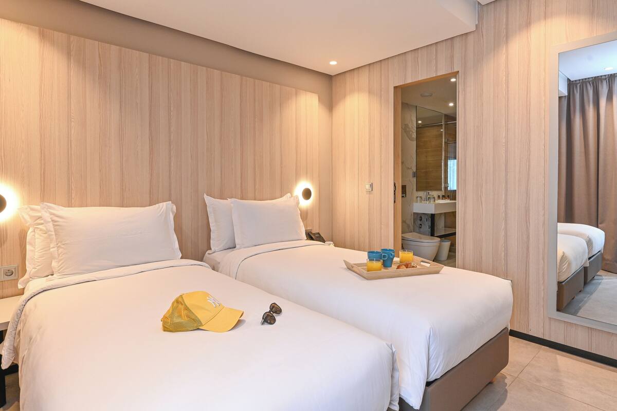 A hotel room with two beds, a mirror, a tray with breakfast items, and a yellow hat on the bed.