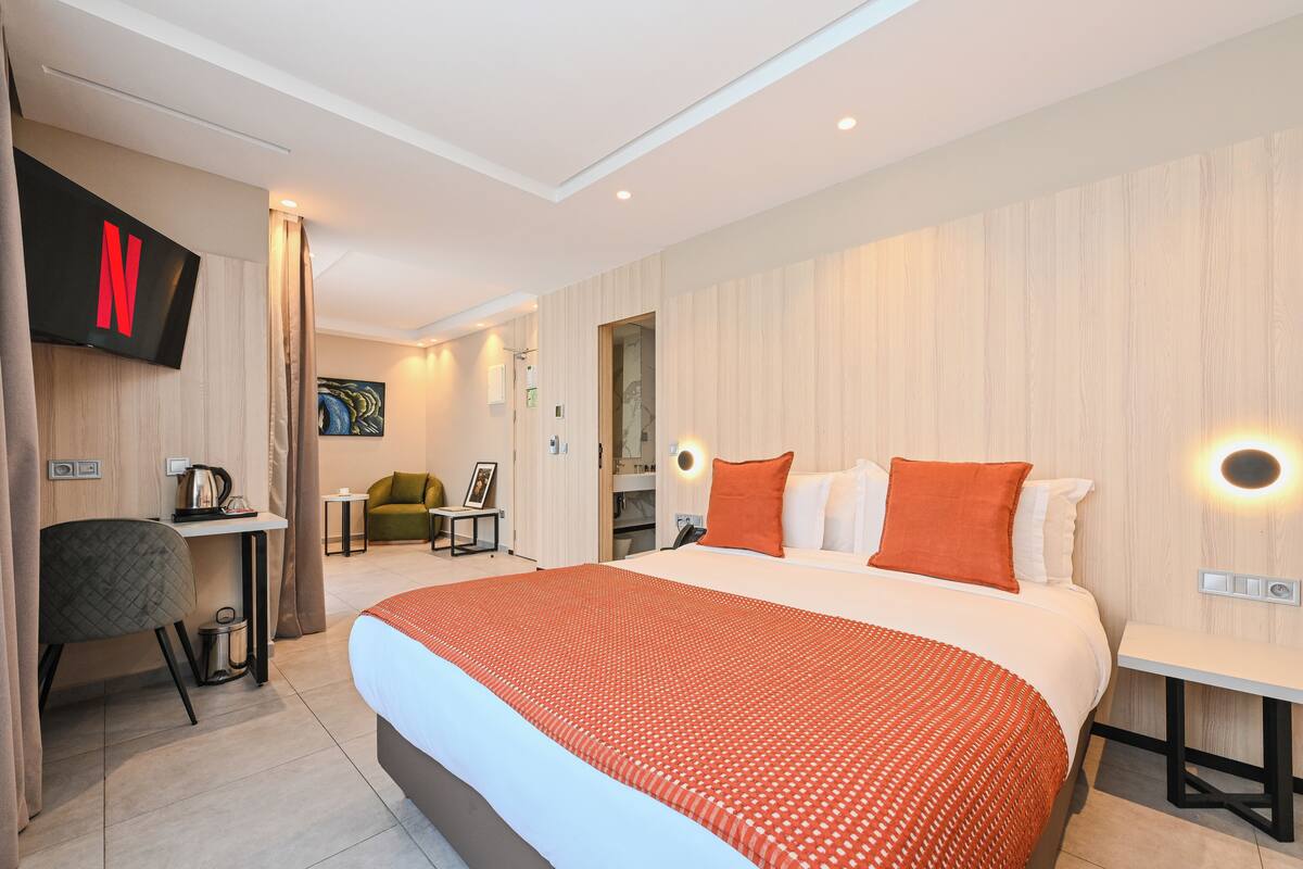 A modern hotel room with a large bed, a desk, a chair, a TV, and a painting on the wall.