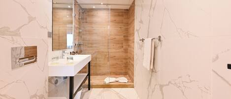 A modern bathroom with a glass shower enclosure, a white sink, and a marble-tiled floor.