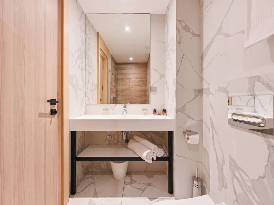 Un baño moderno con puerta de madera, pared de mármol, lavabo con espejo, toallero y zona de ducha.