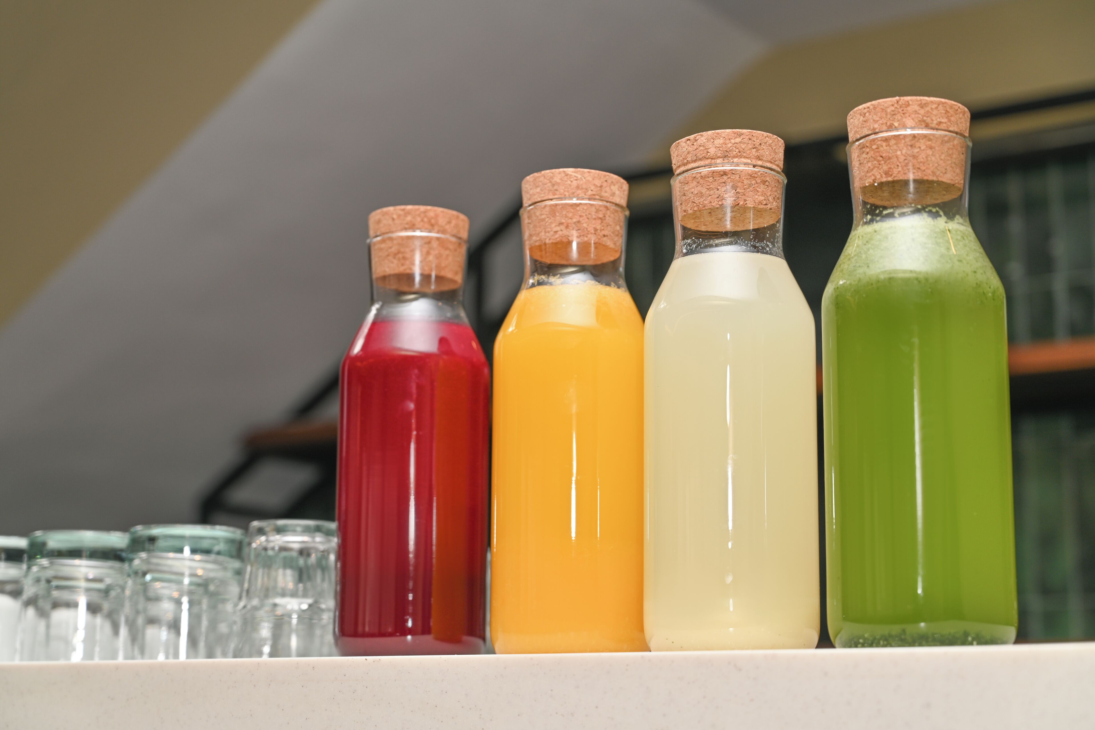 Quatre bouteilles en verre, fermées par des bouchons en liège, sont alignées sur une étagère, chacune contenant un liquide de couleur différente.