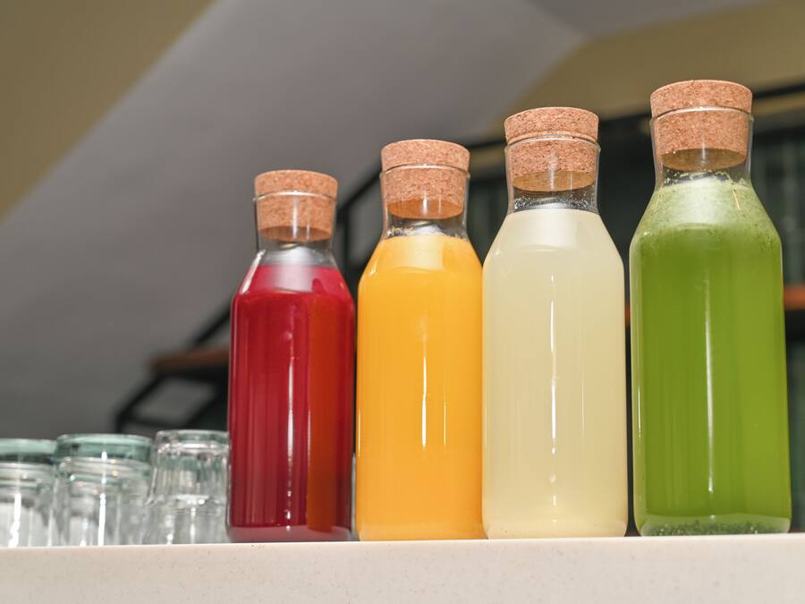 Four glass bottles with cork stoppers, each containing a different colored liquid, lined up on a shelf.