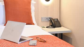 Ett hotellrum med en säng, en bärbar dator, en telefon och en väggmonterad lampa.