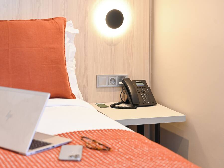 Ett hotellrum med en säng, en bärbar dator, en telefon och en väggmonterad lampa.