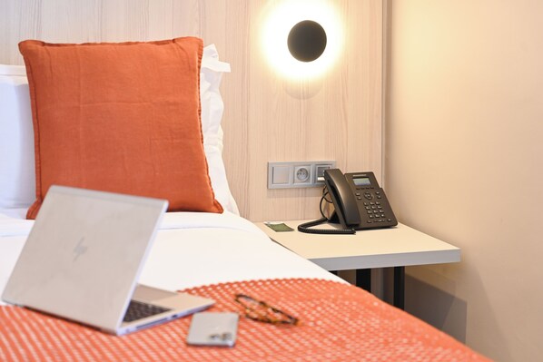 Ein Hotelzimmer mit einem Bett, einem Laptop, einem Telefon und einer Wandleuchte.